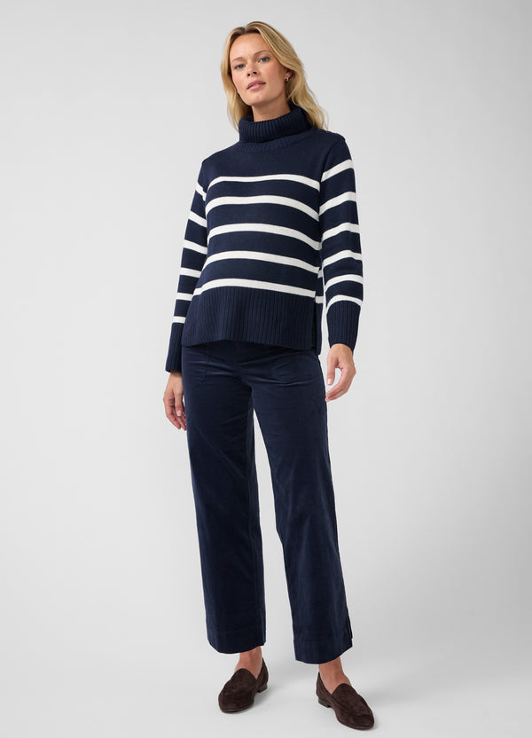 A pregnant woman modeling a navy blue knit maternity sweater with white horizontal stripes and matching navy wide-leg maternity trousers, paired with dark brown slip-on shoes, against a light gray studio background.