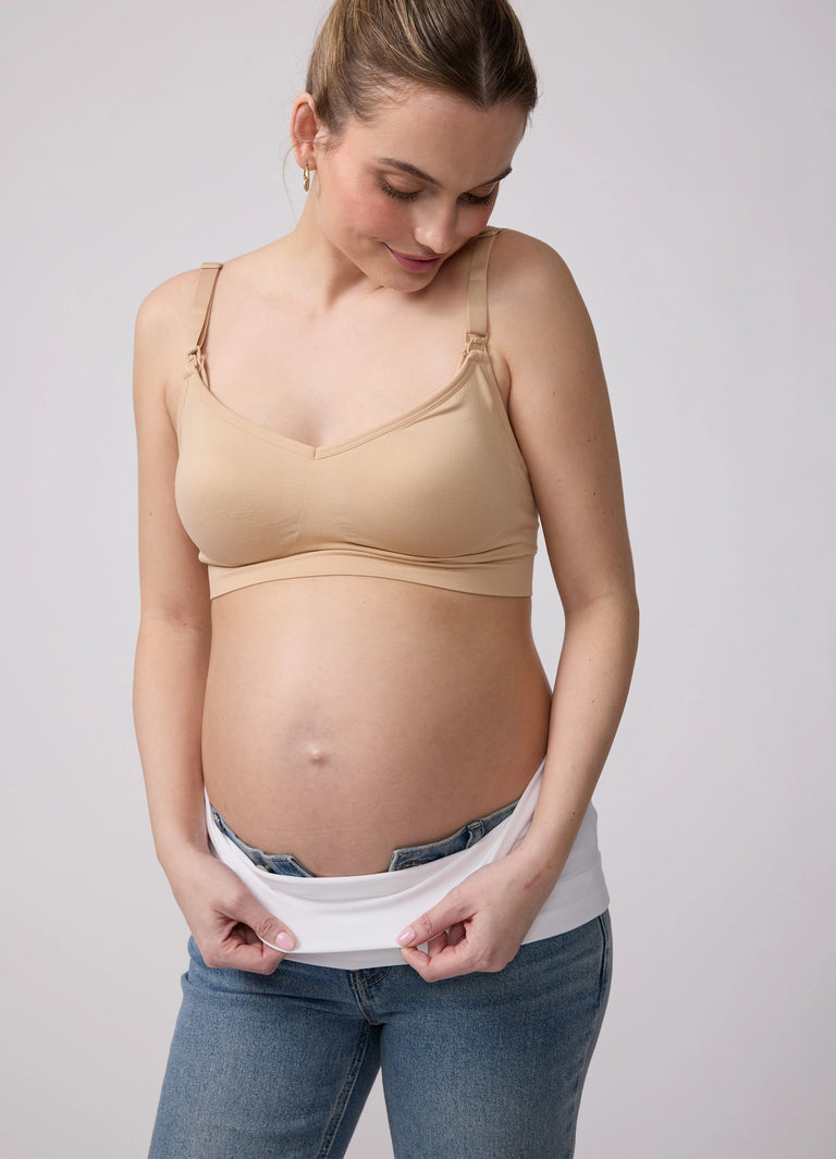 ||Pregnant woman wearing a beige bra, white Bellaband, and blue jeans on a white background