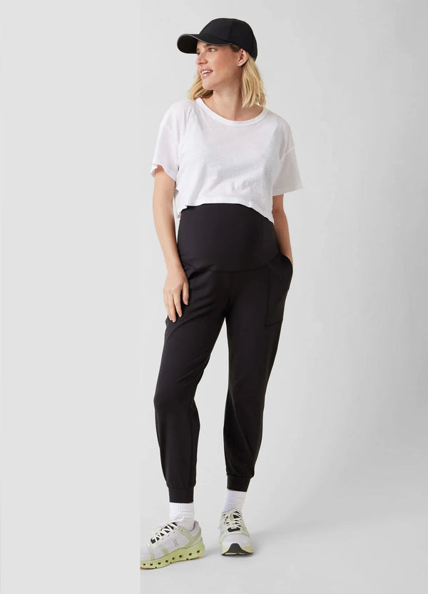 ||Pregnant woman wearing a white t-shirt, black joggers, and a black cap on a white background