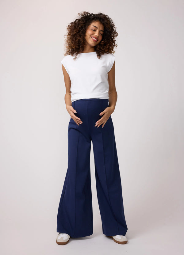 ||A pregnant woman wearing a navy blue flare ponte knit maternity pants and a white shirt with white sneakers