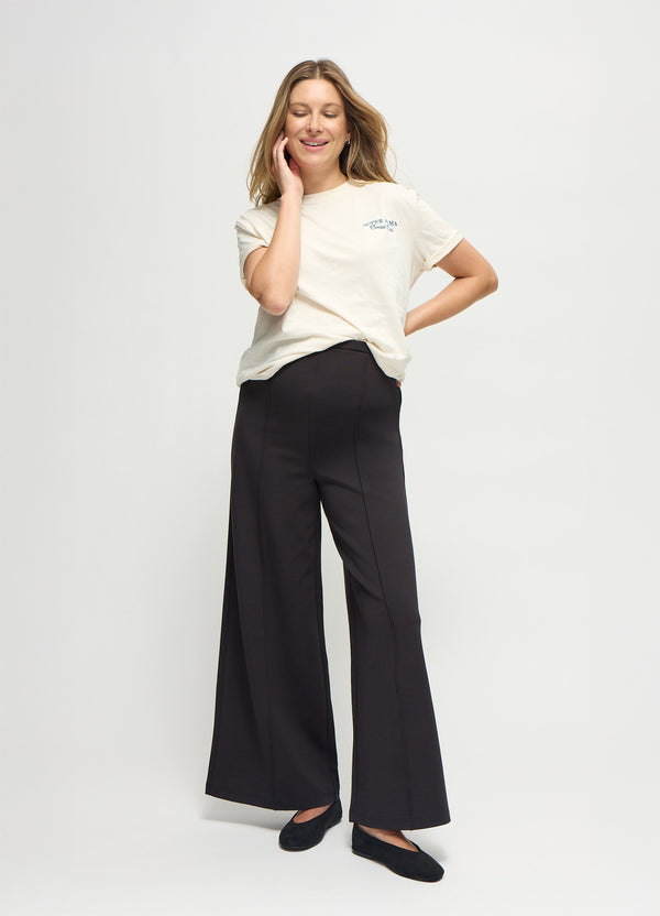 A pregnant woman wearing a black flare ponte knit maternity pants, a white shirt, and black flats