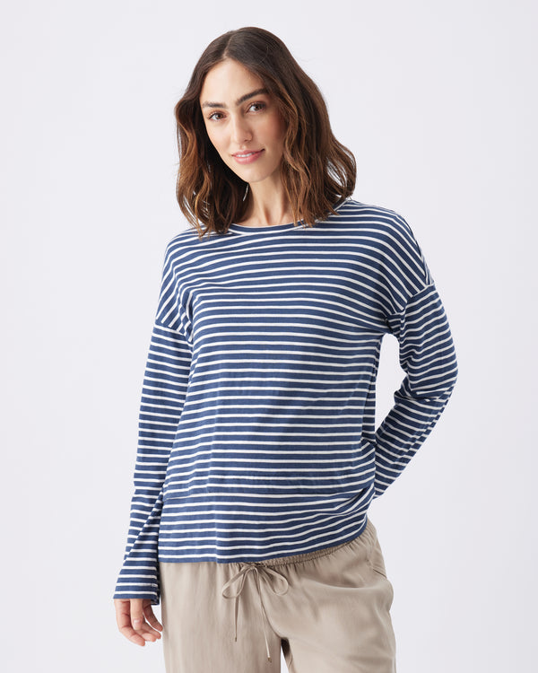 A half body shot of a woman wearing a navy blue and white long sleeve striped nursing top with beige pants