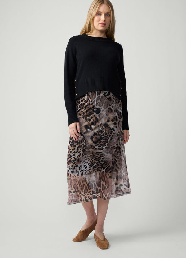 A pregnant woman wearing a black knit sweater and an animal-print mesh midi skirt with brown suede ballet flats