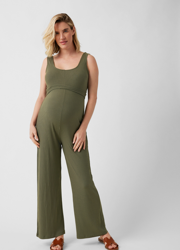 A pregnant woman wearing a rib knit olive jumpsuit with brown flat sandals