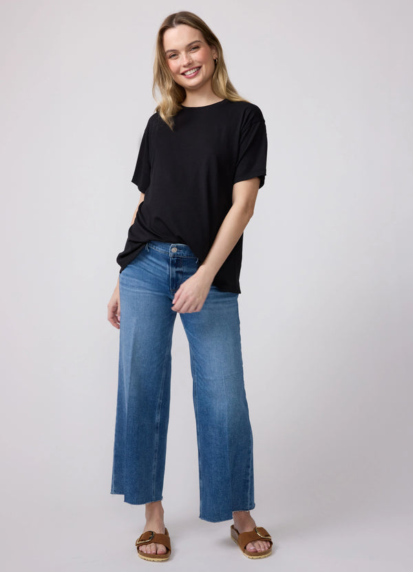 A pregnant woman wearing a black short sleeve relaxed jersey maternity tee and blue denim jeans with brown slides