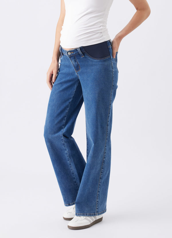 A pregnant woman wearing blue wide leg jeans with a white top and white sneakers