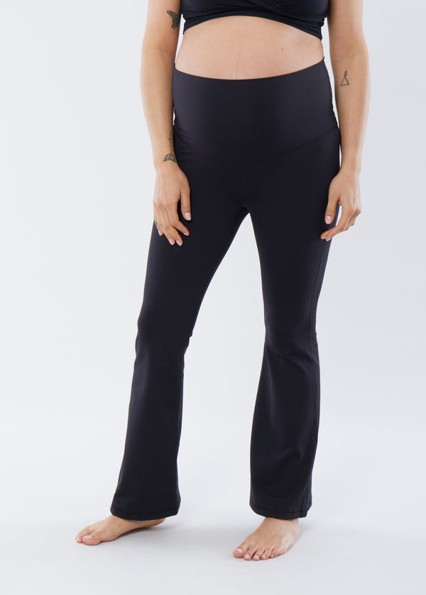 ||A pregnant woman wearing a pair of black flare maternity leggings with a fold-down waistband.