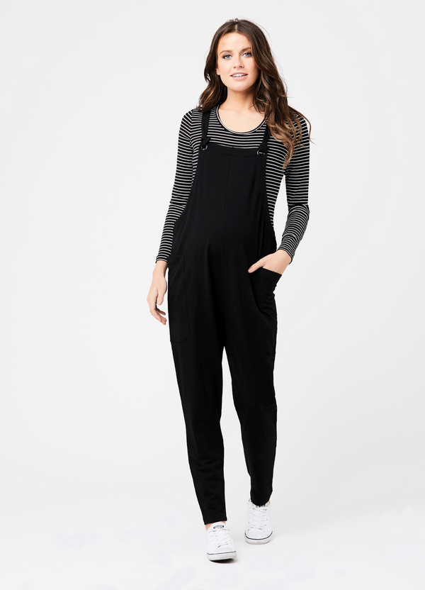 A pregnant woman wearing a black overall jumpsuit with a striped top underneath against a white background